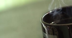 Steaming coffee cup with green background.